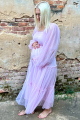 woman wearing a light pink maternity dress with long sleeves and tiered ruffle details, holding her baby bump