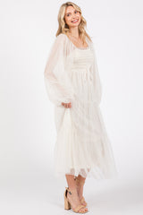 woman wearing a white smocked midi dress with sheer sleeves and a tiered skirt, smiling and standing sideways