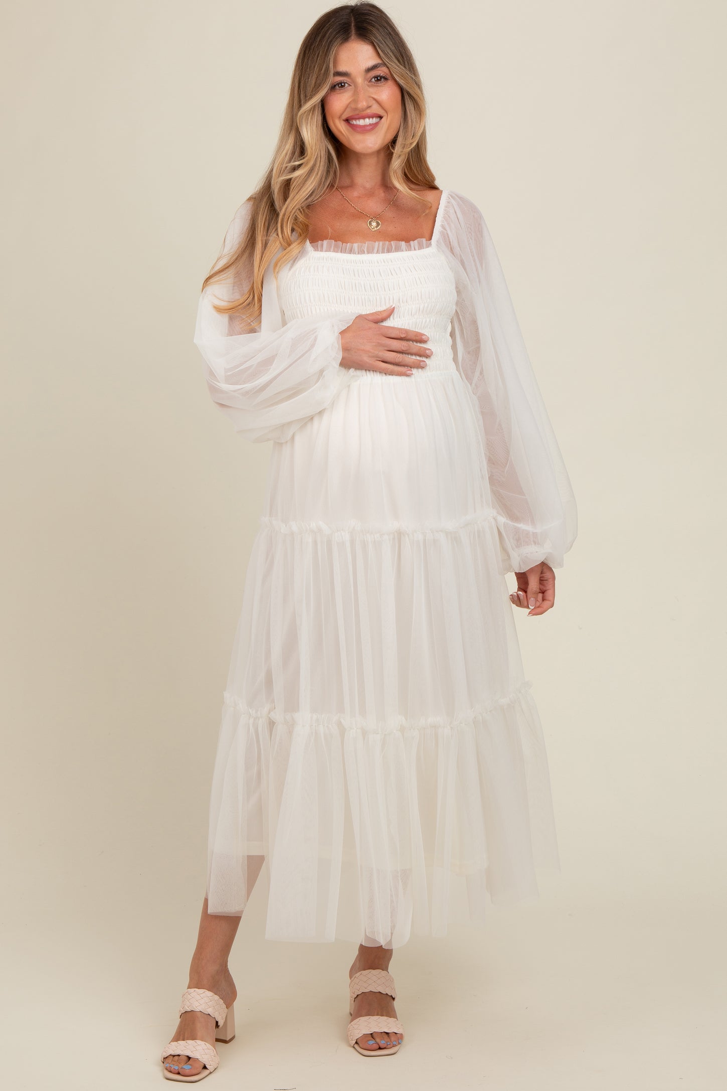 woman wearing a white maternity maxi dress with puffed sleeves and tiered tulle, holding her baby bump