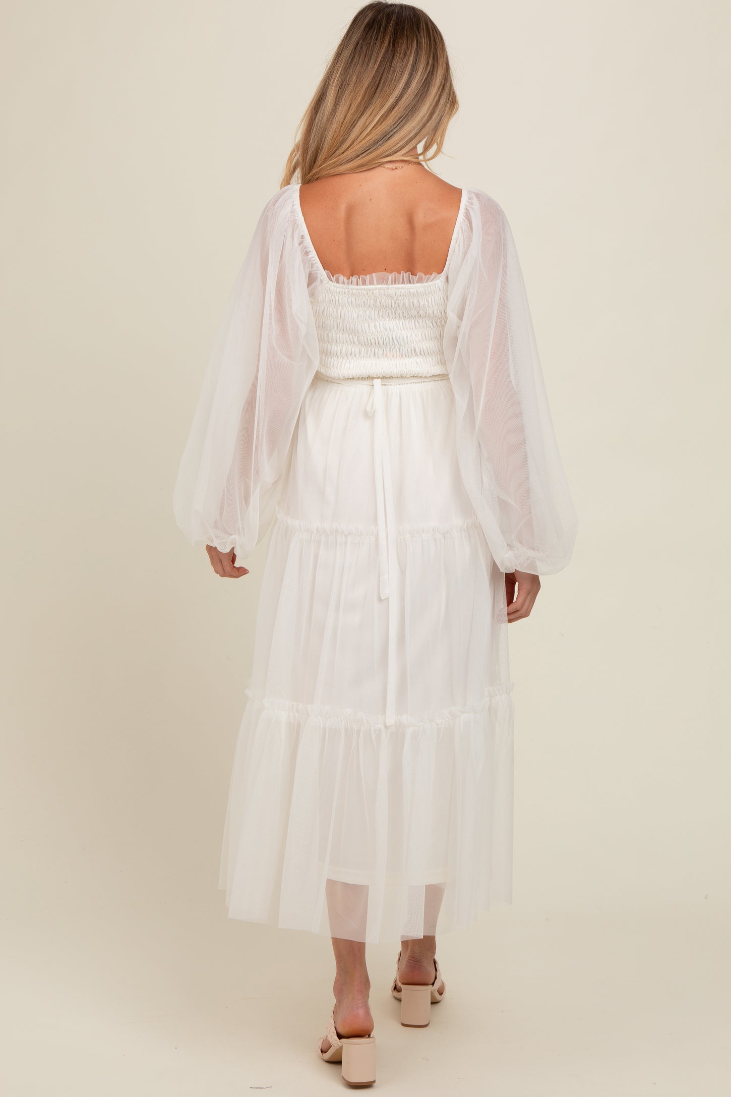 woman wearing a white maternity dress with a smocked bodice and sheer puff sleeves, showing the back view