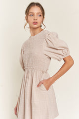 woman wearing a beige plaid puff sleeve dress with smocked bodice and side pockets
