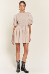 woman wearing a beige smocked mini dress with puff sleeves and black western boots