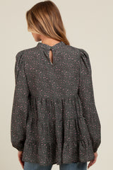 woman wearing a dark gray maternity top with a tiered design and colorful print, showing a keyhole detail at the back