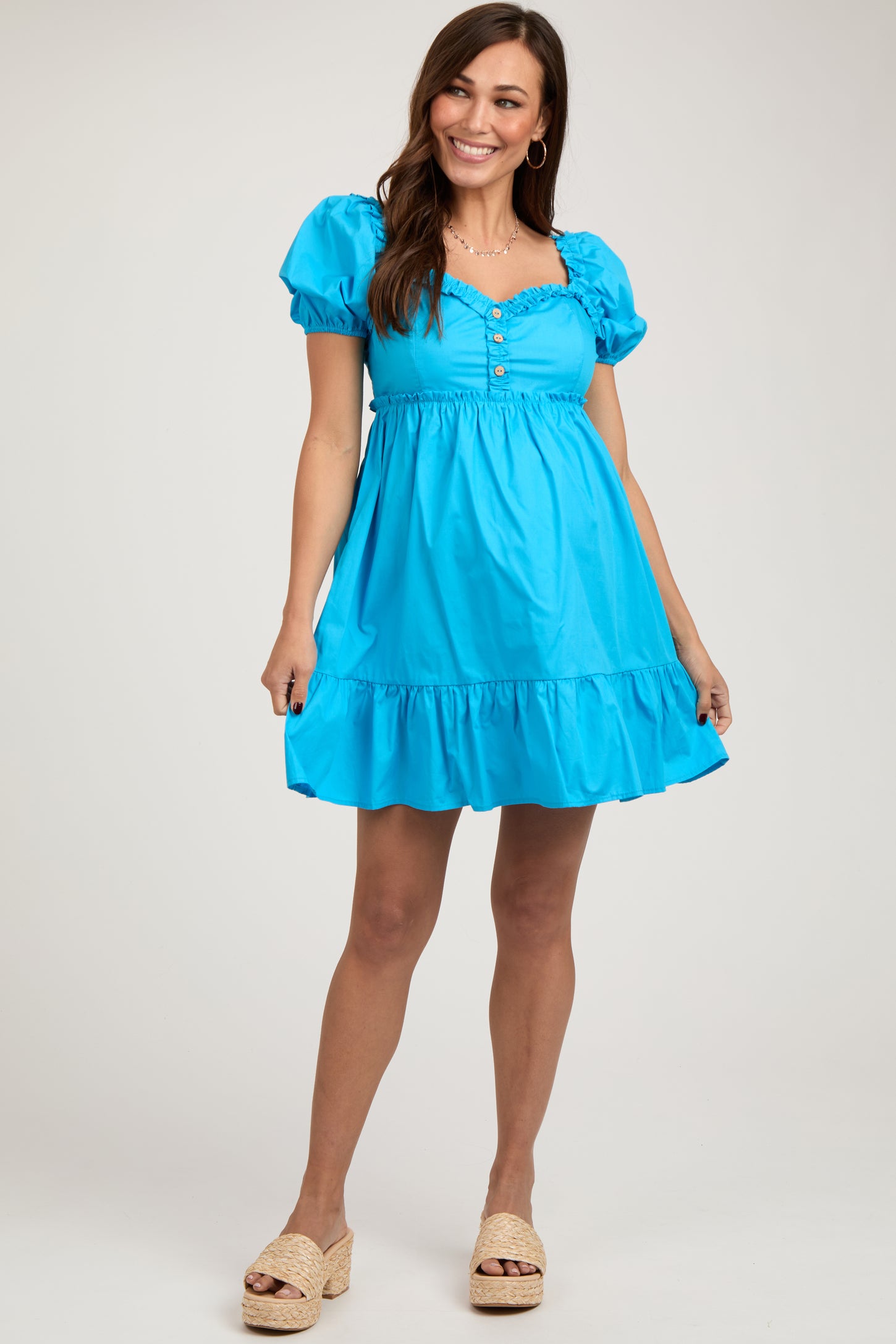 woman wearing a bright blue short sleeve maternity dress with a button detail and ruffle hem