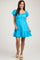 woman wearing a bright blue maternity dress with puff sleeves and a tiered skirt, smiling at the camera.