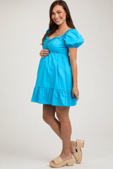 woman wearing a bright blue maternity dress with puff sleeves and a tiered ruffle hem, showing her baby bump