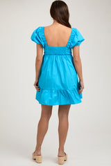 woman wearing a bright blue maternity dress with short puff sleeves and a ruffled hem, showcasing a smocked back.