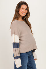 woman wearing a beige maternity sweater with striped sleeves and a visible baby bump