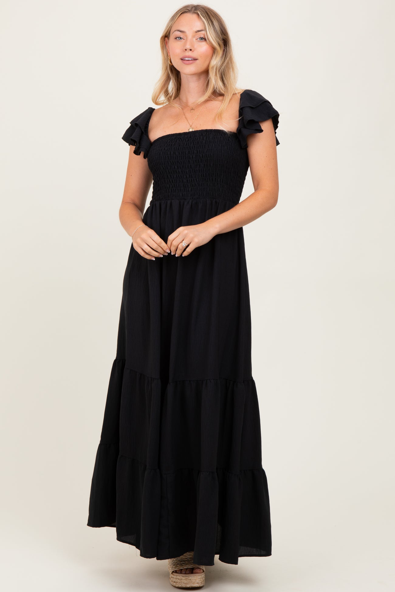 woman wearing a black strapless maxi dress with ruffled sleeves and a tiered skirt