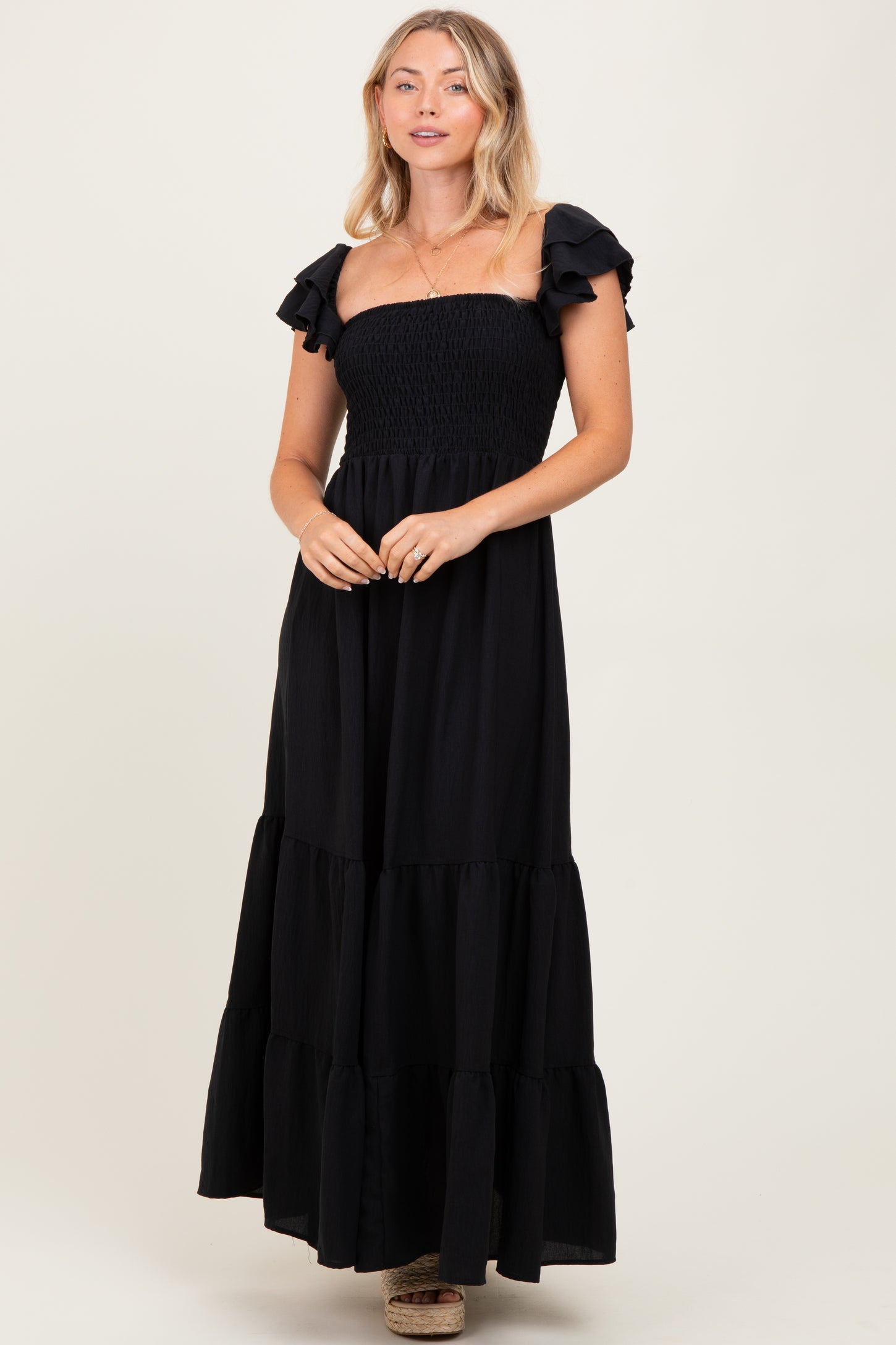 woman wearing a black strapless maxi dress with ruffled sleeves and a tiered skirt