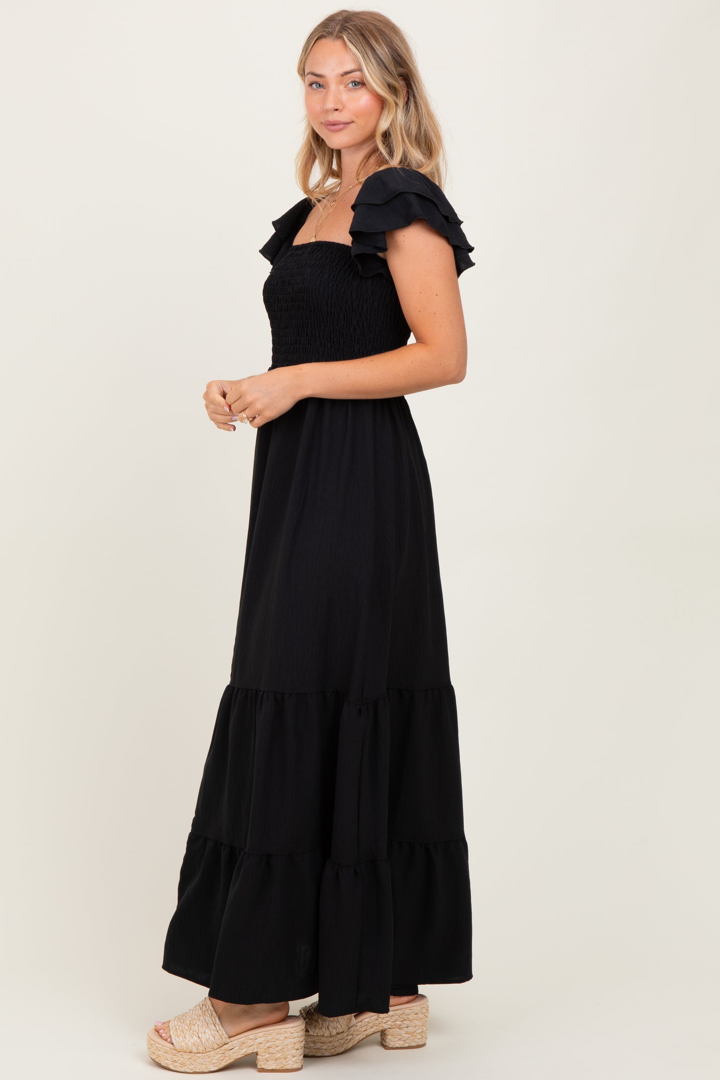 woman wearing a black maxi dress with ruffled sleeves and a tiered skirt, standing in profile