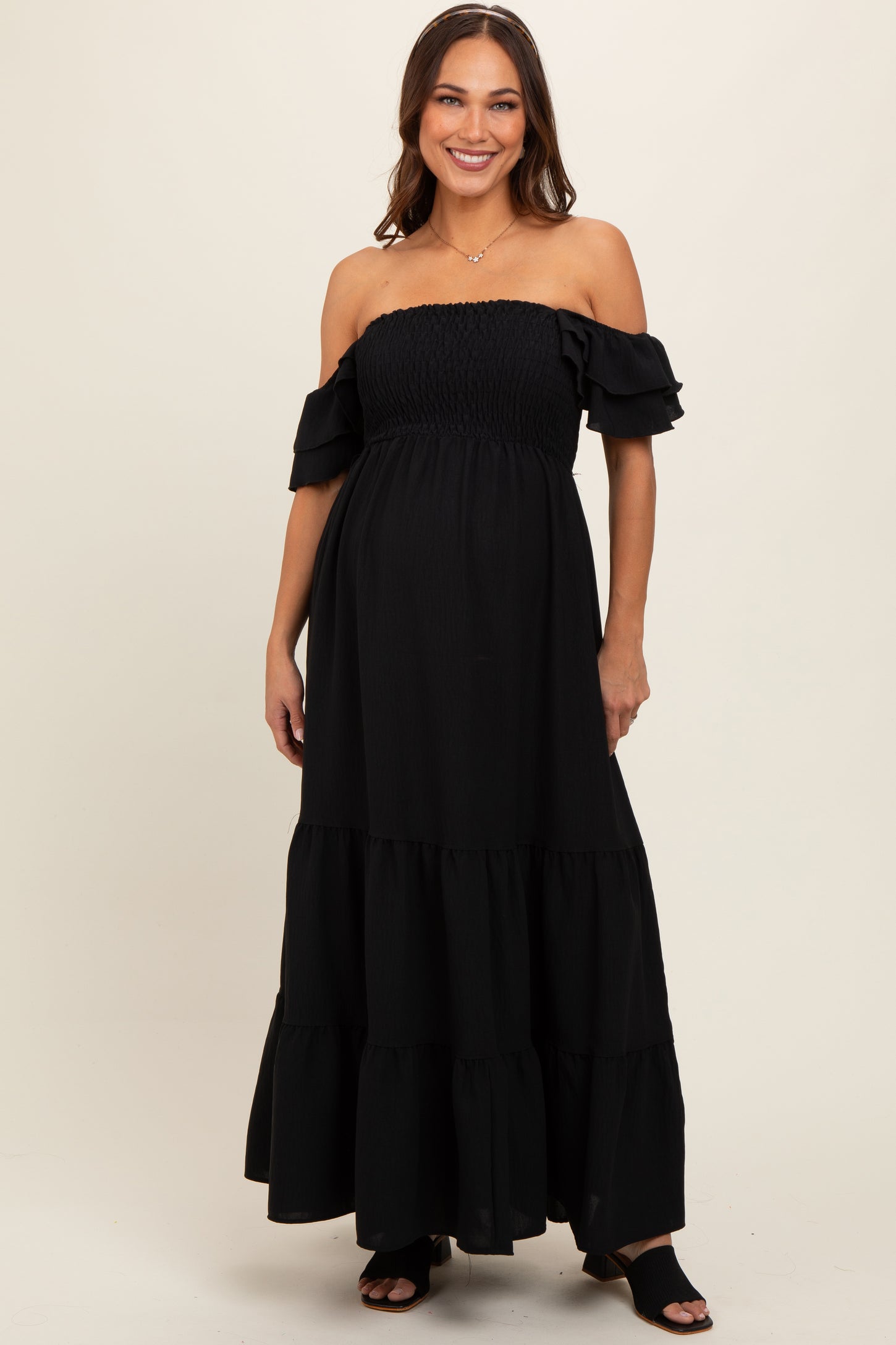 woman wearing a black off-the-shoulder maternity maxi dress with ruffle details and a visible baby bump