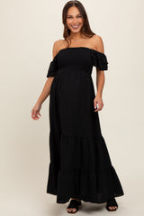 woman wearing a black off-the-shoulder maternity dress with ruffle sleeves and tiered skirt, showing baby bump
