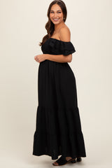 woman wearing a black off-the-shoulder maternity maxi dress with ruffled sleeves and tiered skirt, showing her baby bump