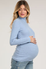 woman wearing a light blue turtleneck maternity top and holding her baby bump