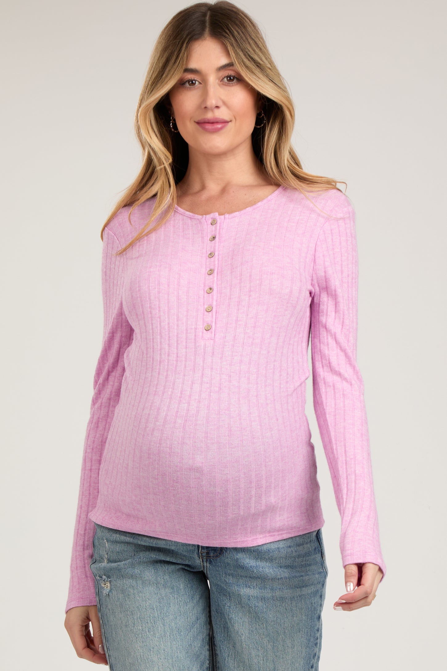 woman wearing a light pink ribbed maternity top with button details and a visible baby bump