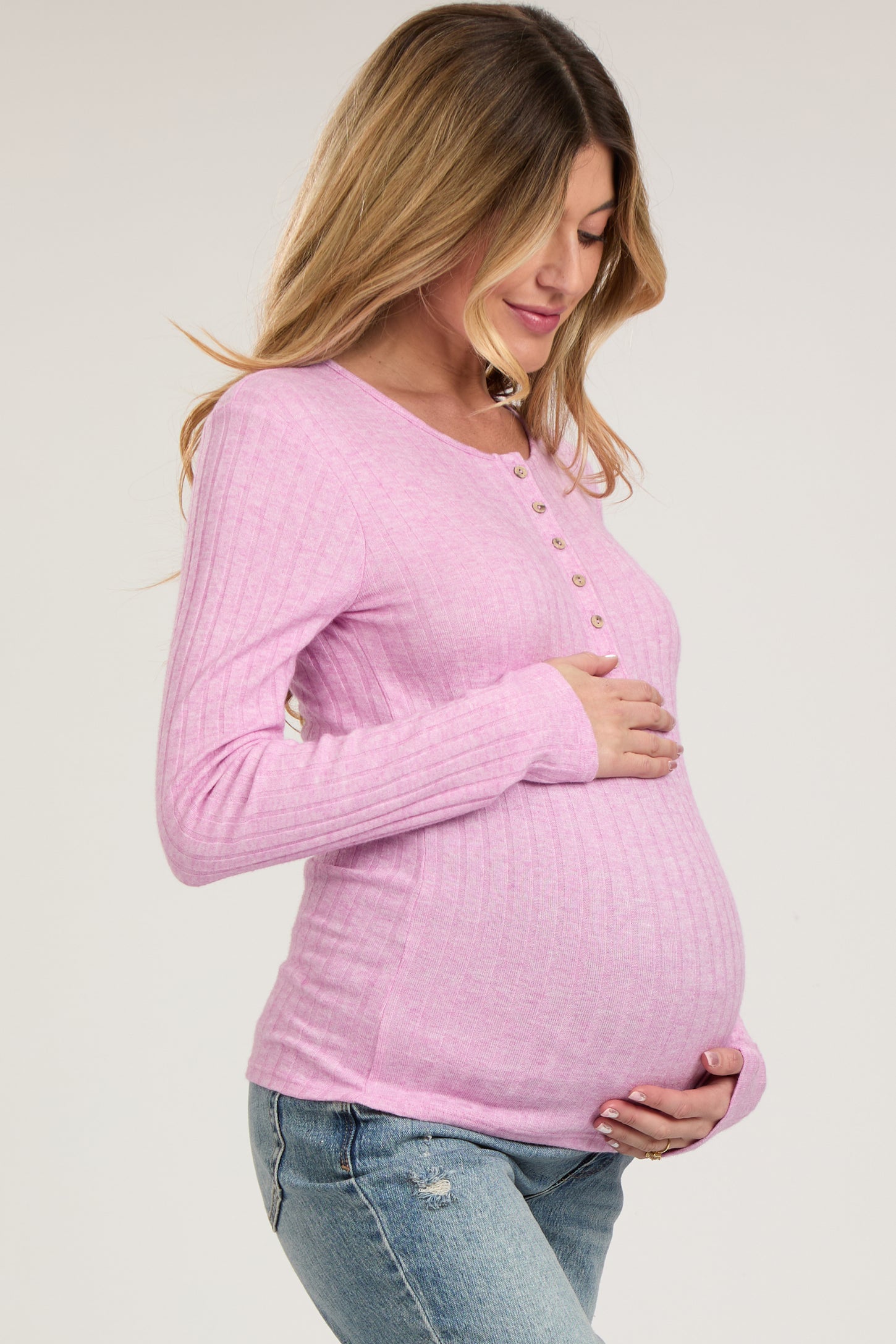 woman wearing a light pink maternity long sleeve top with buttons and holding her baby bump