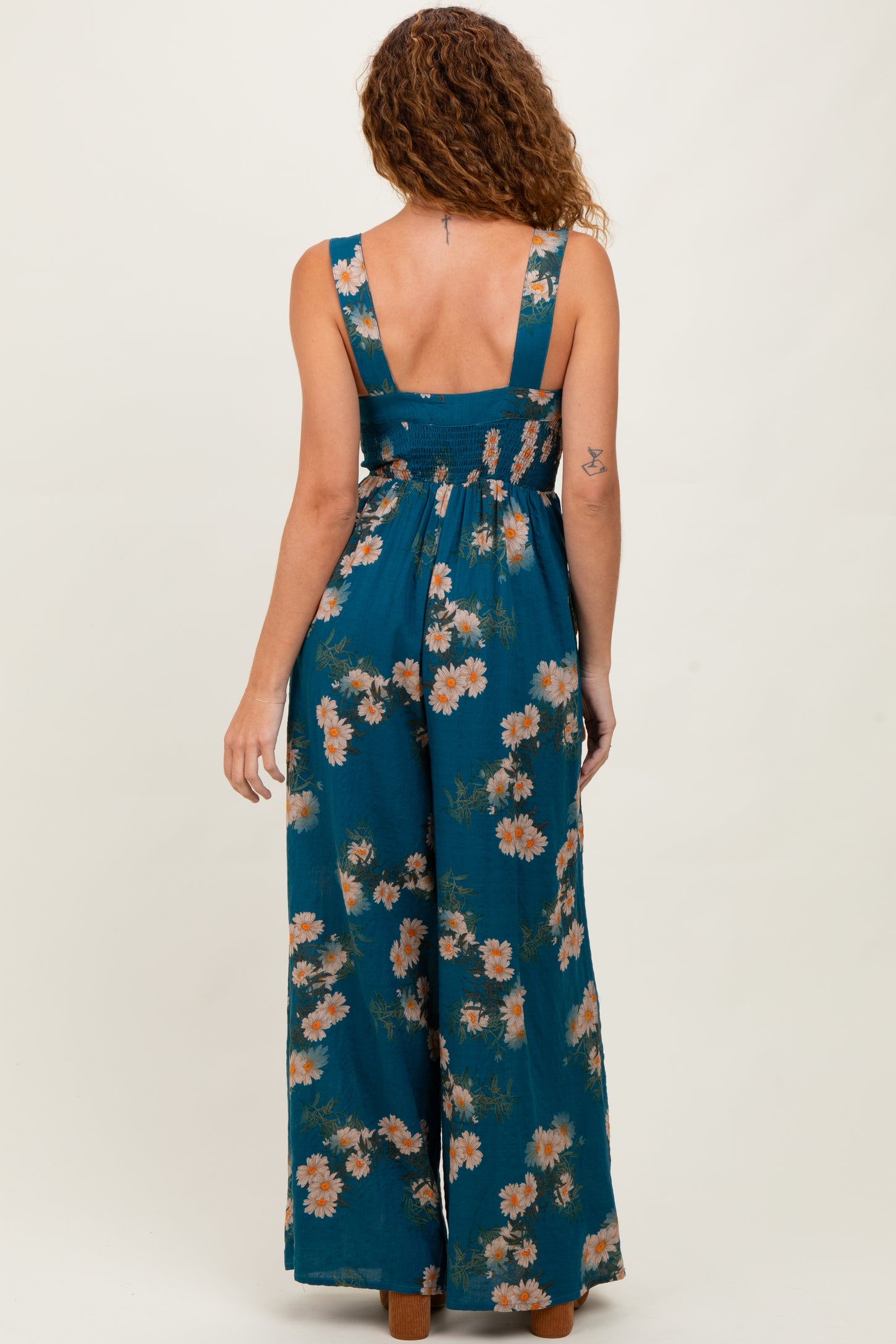 woman wearing a teal floral maxi dress with a smocked back and wide leg pants, standing with her back to the camera