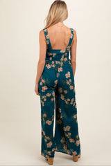 woman wearing a teal floral maternity jumpsuit with a deep back and wide legs, showcasing a baby bump