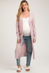 woman wearing a light pink long cardigan over a white tank top and blue jeans, showing her baby bump