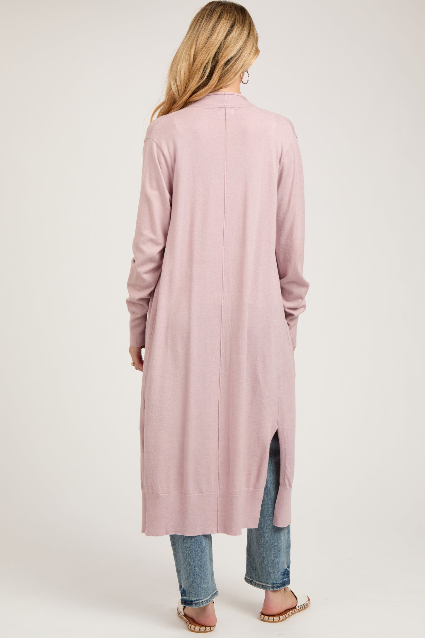 woman wearing a dusty pink long sleeve maternity cardigan with side slits and paired with jeans