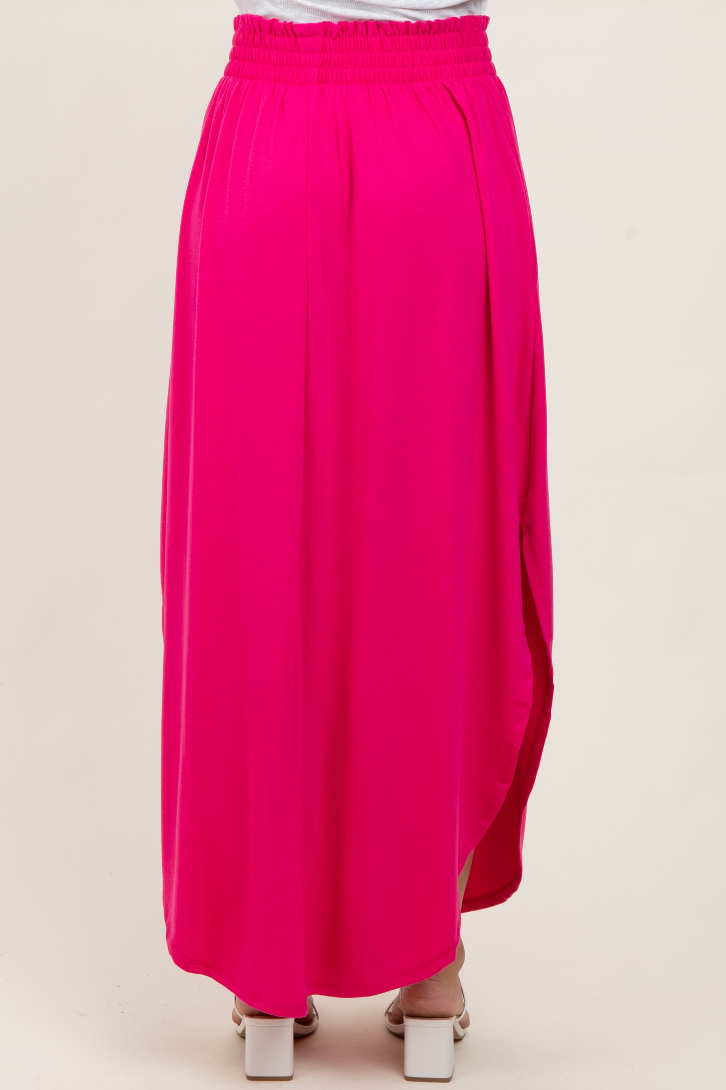 woman wearing a hot pink maxi skirt with a gathered waistband and a side slit, viewed from the back