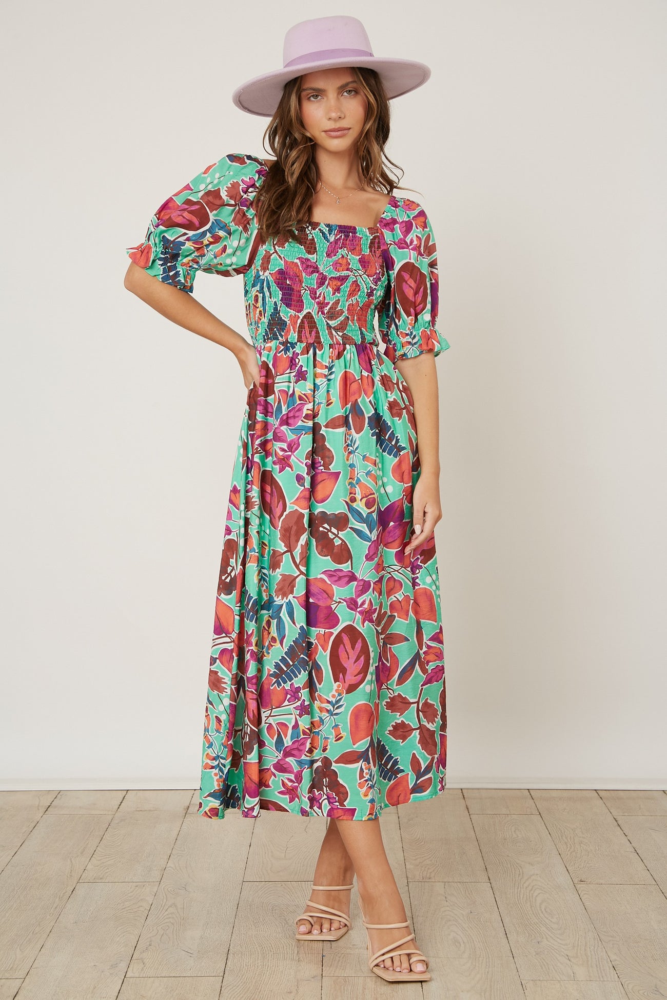 woman wearing a colorful floral maxi dress with puff sleeves and a square neckline, paired with a light purple hat