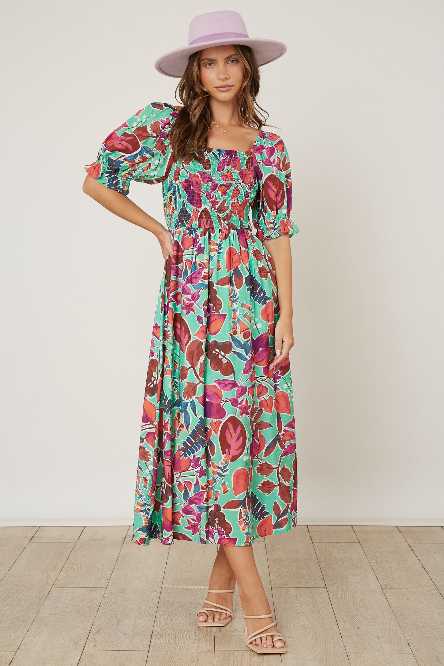 woman wearing a colorful floral maxi dress with puff sleeves and a square neckline, paired with a light purple hat