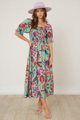 woman wearing a colorful floral maxi dress with puff sleeves and a square neckline, paired with a light purple hat