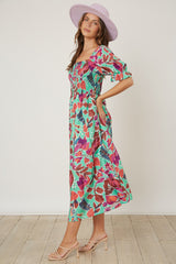 woman wearing a floral print midi dress with puff sleeves and a square neckline, paired with a wide-brimmed pink hat