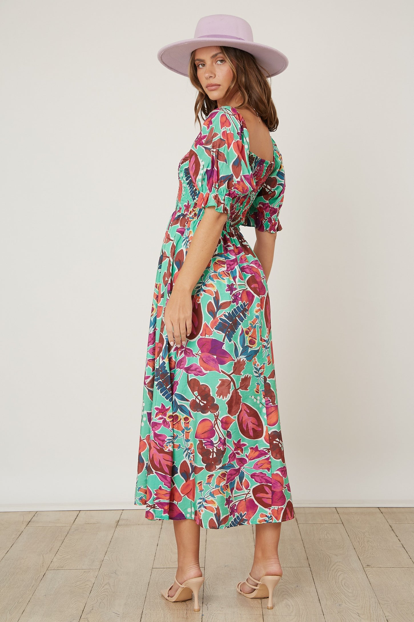 woman wearing a vibrant floral print maxi dress with puff sleeves and a cinched waist, paired with a wide-brimmed hat