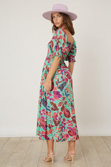 woman wearing a vibrant floral print maxi dress with puff sleeves and a cinched waist, paired with a wide-brimmed hat