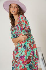 woman wearing a floral print maxi dress in green and pink with puff sleeves and a wide-brimmed pink hat