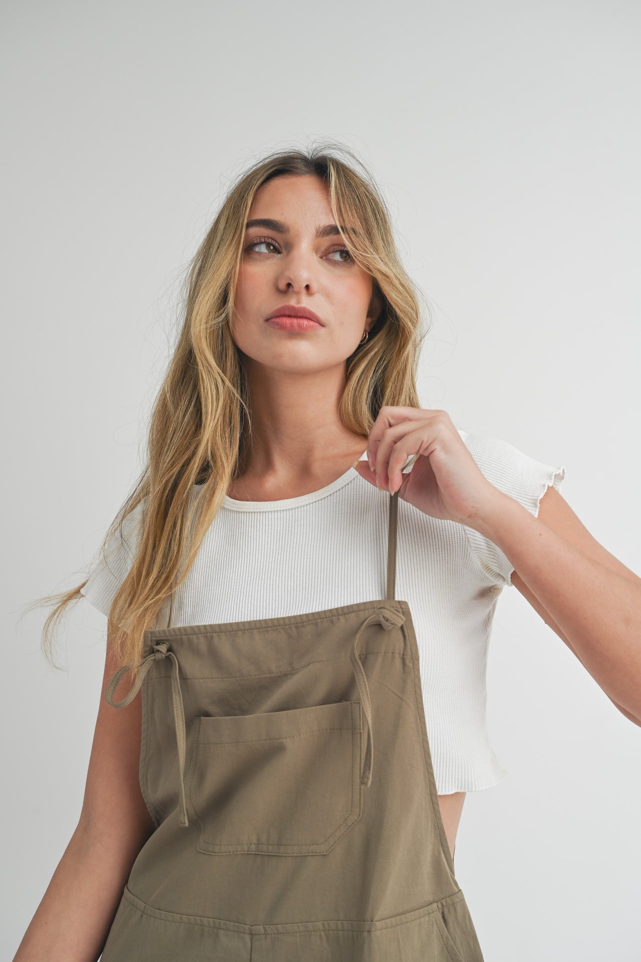 woman wearing a white cropped ribbed t-shirt under a khaki apron dress with adjustable straps