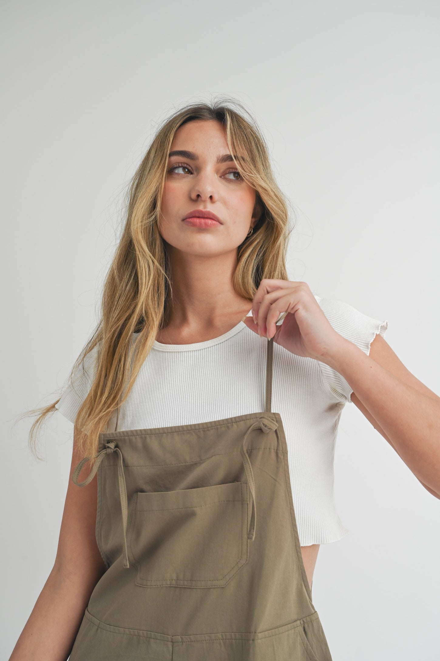 woman wearing a white cropped ribbed t-shirt under a khaki apron dress with adjustable straps