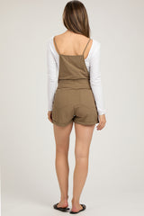 woman wearing a brown maternity overall shorts jumpsuit with a white long sleeve top, styled casually