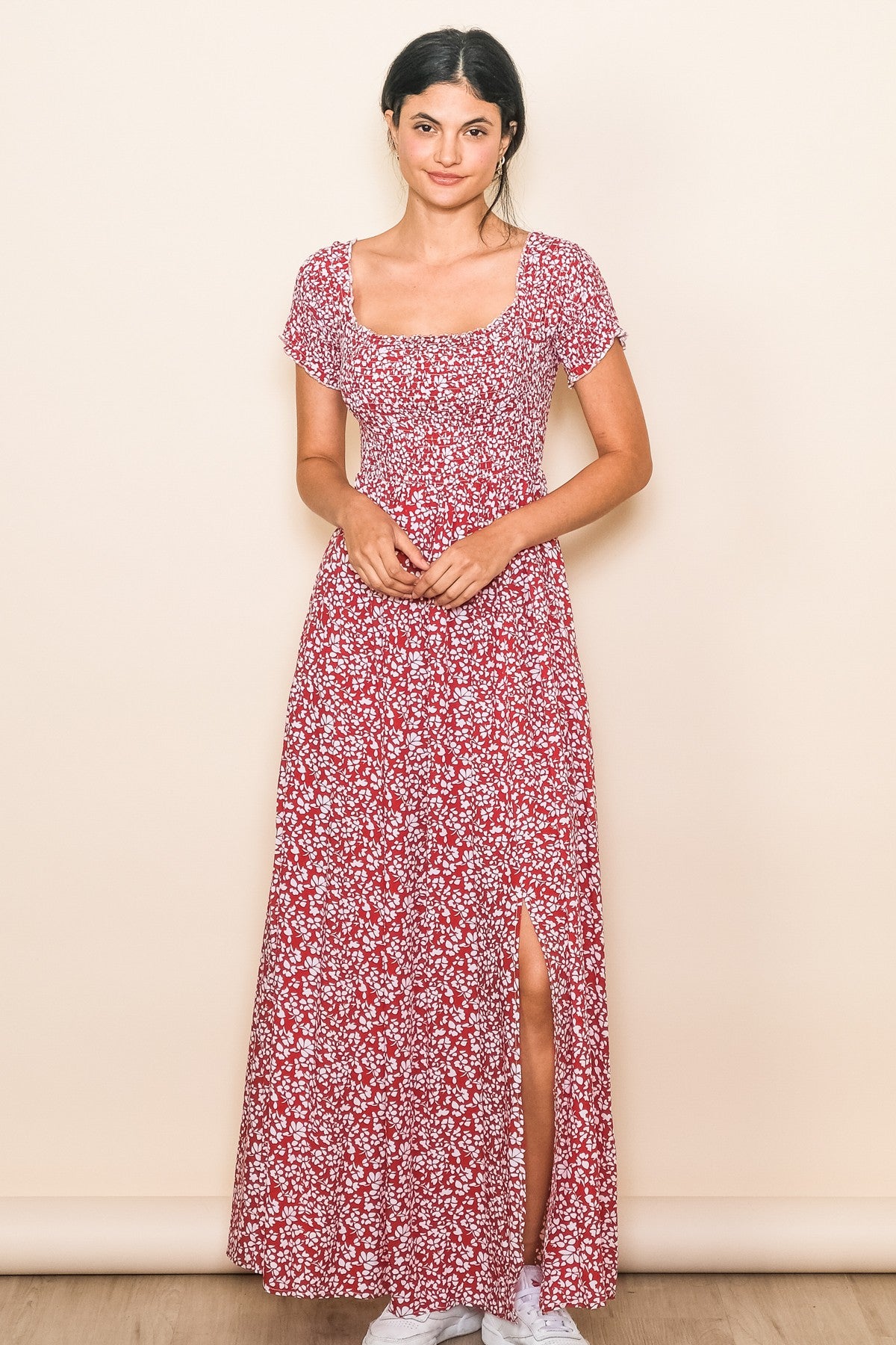 woman wearing a red floral maxi dress with short sleeves and a thigh-high slit, standing against a neutral background