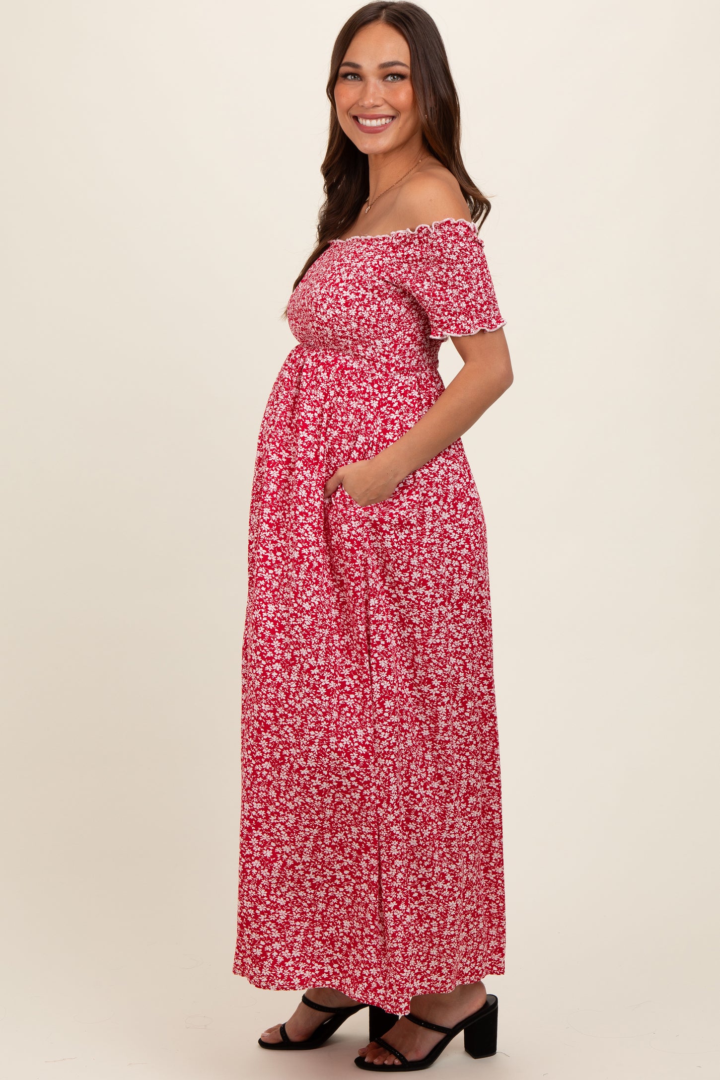 woman wearing a red floral off-shoulder maternity dress with pockets and a visible baby bump