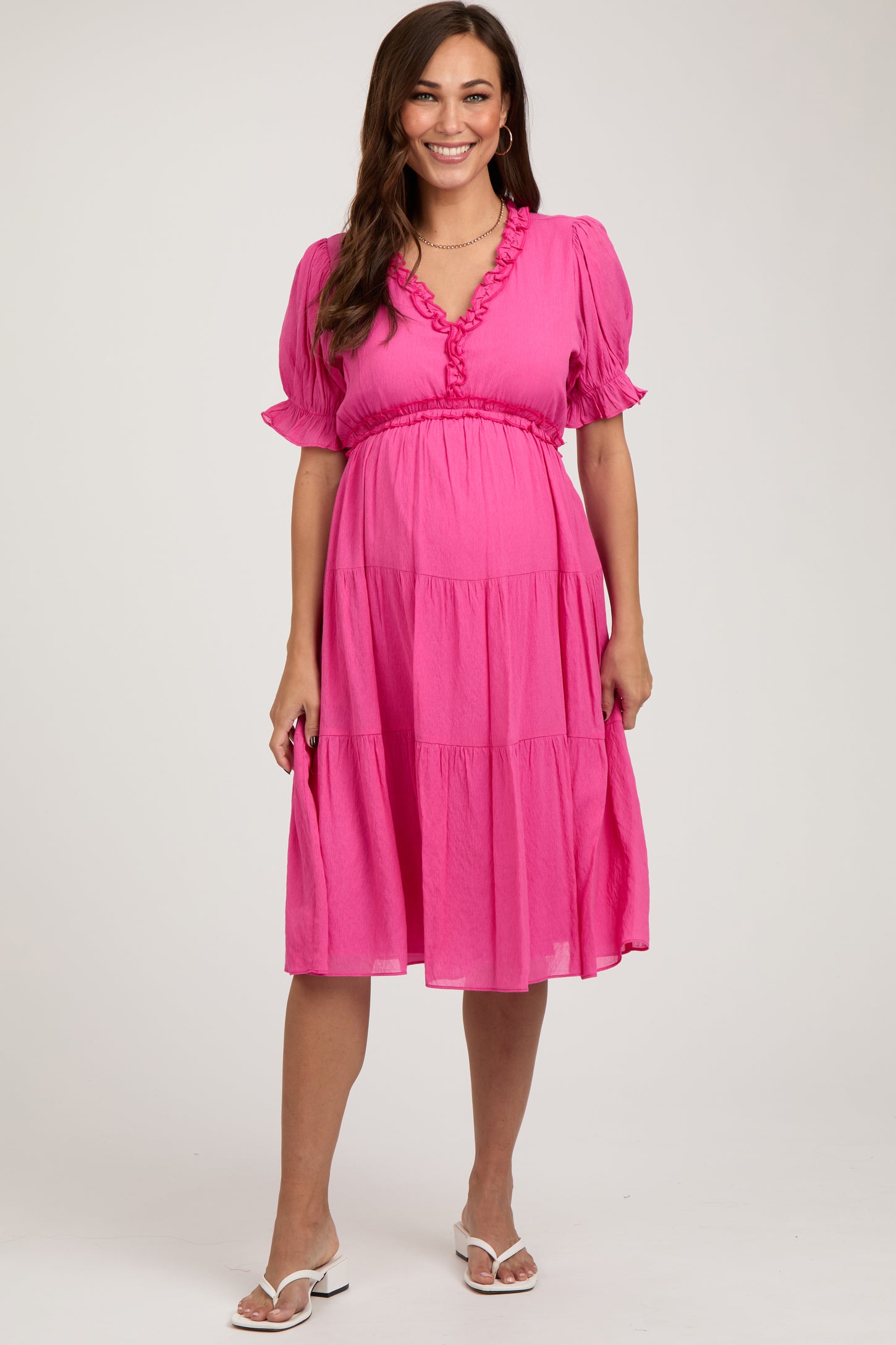 woman wearing a bright pink maternity dress with puff sleeves and a tiered skirt, showing her baby bump