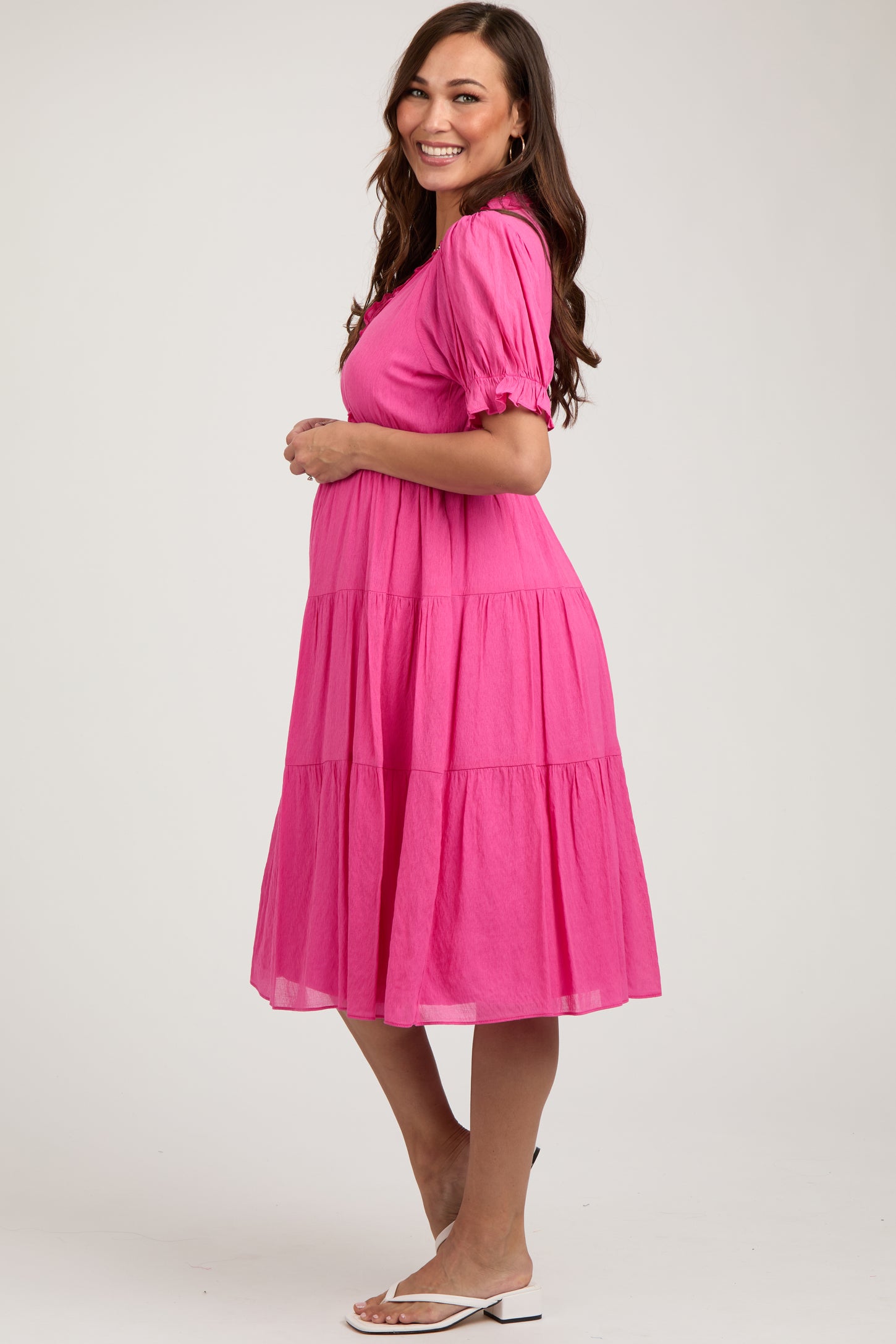 woman wearing a bright pink maternity dress with short puff sleeves and tiered design, showing her baby bump