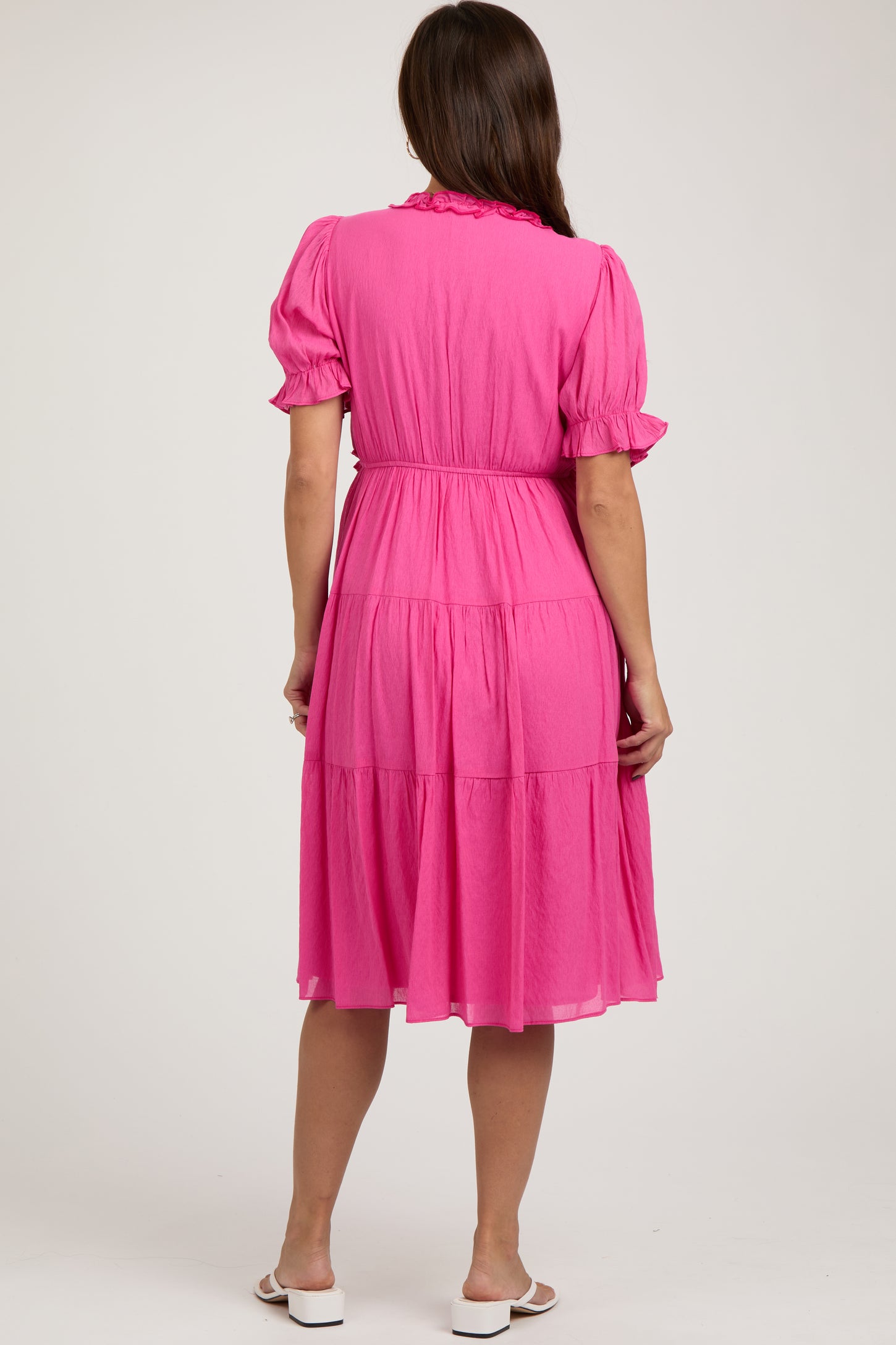 woman wearing a pink maternity dress with short puff sleeves and a tiered skirt, showing her baby bump