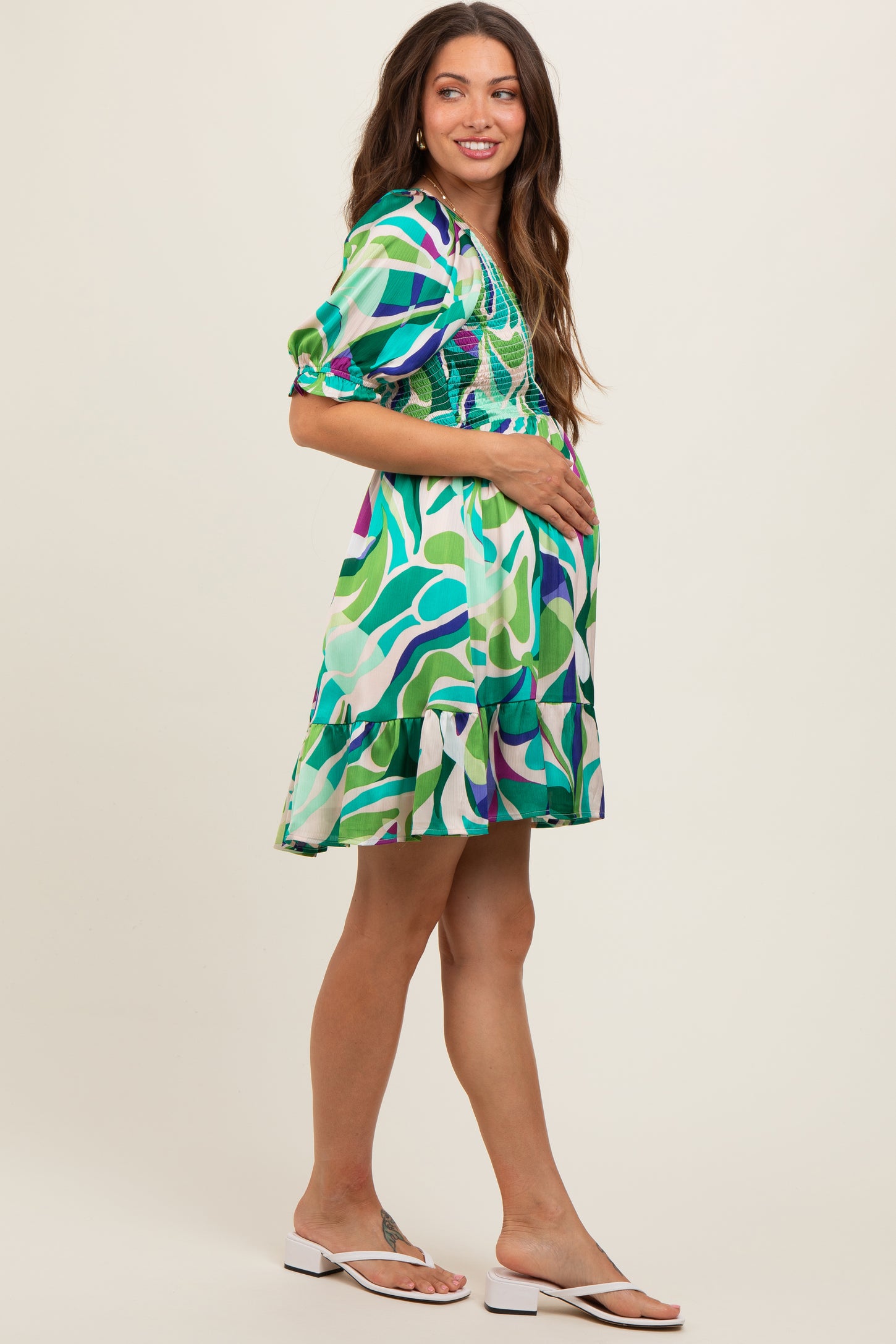 woman wearing a multicolored patterned maternity dress with a ruffled hem and holding her baby bump