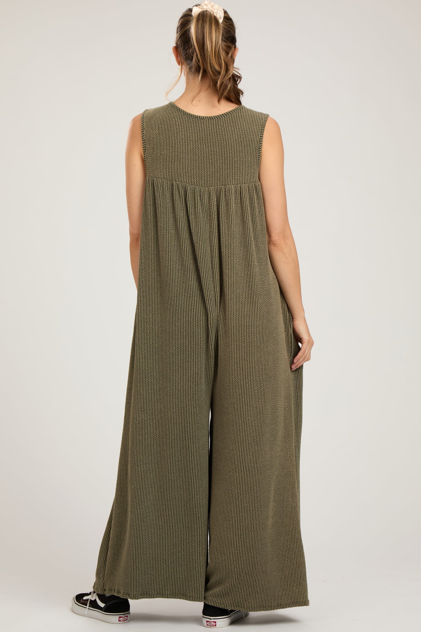 woman wearing a green striped maternity jumpsuit with a loose fit and wide legs, viewed from the back