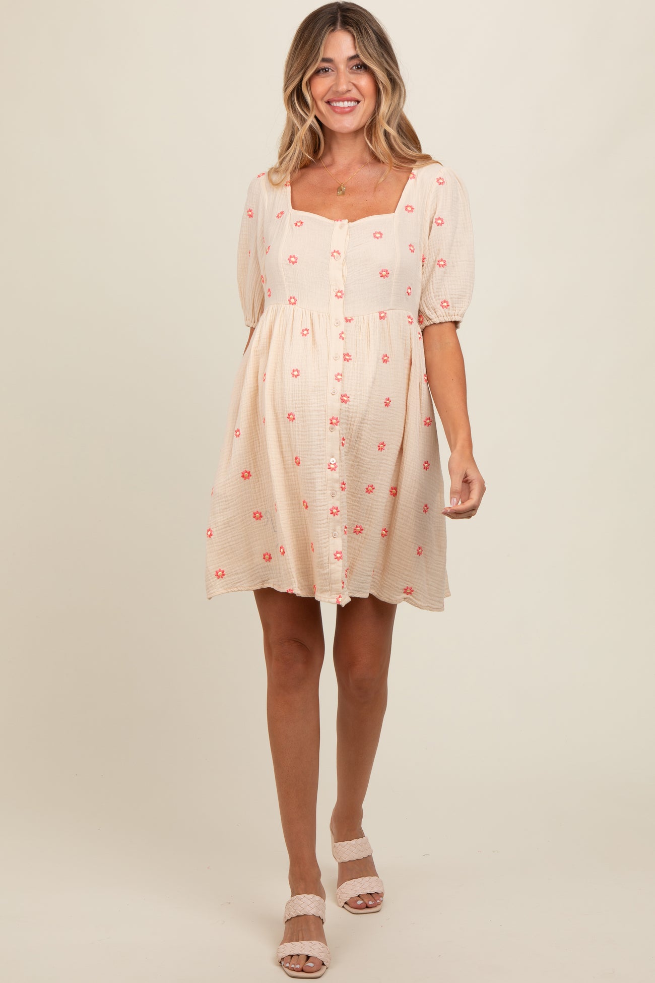 woman wearing a light pink maternity dress with floral prints and puff sleeves, showing a baby bump