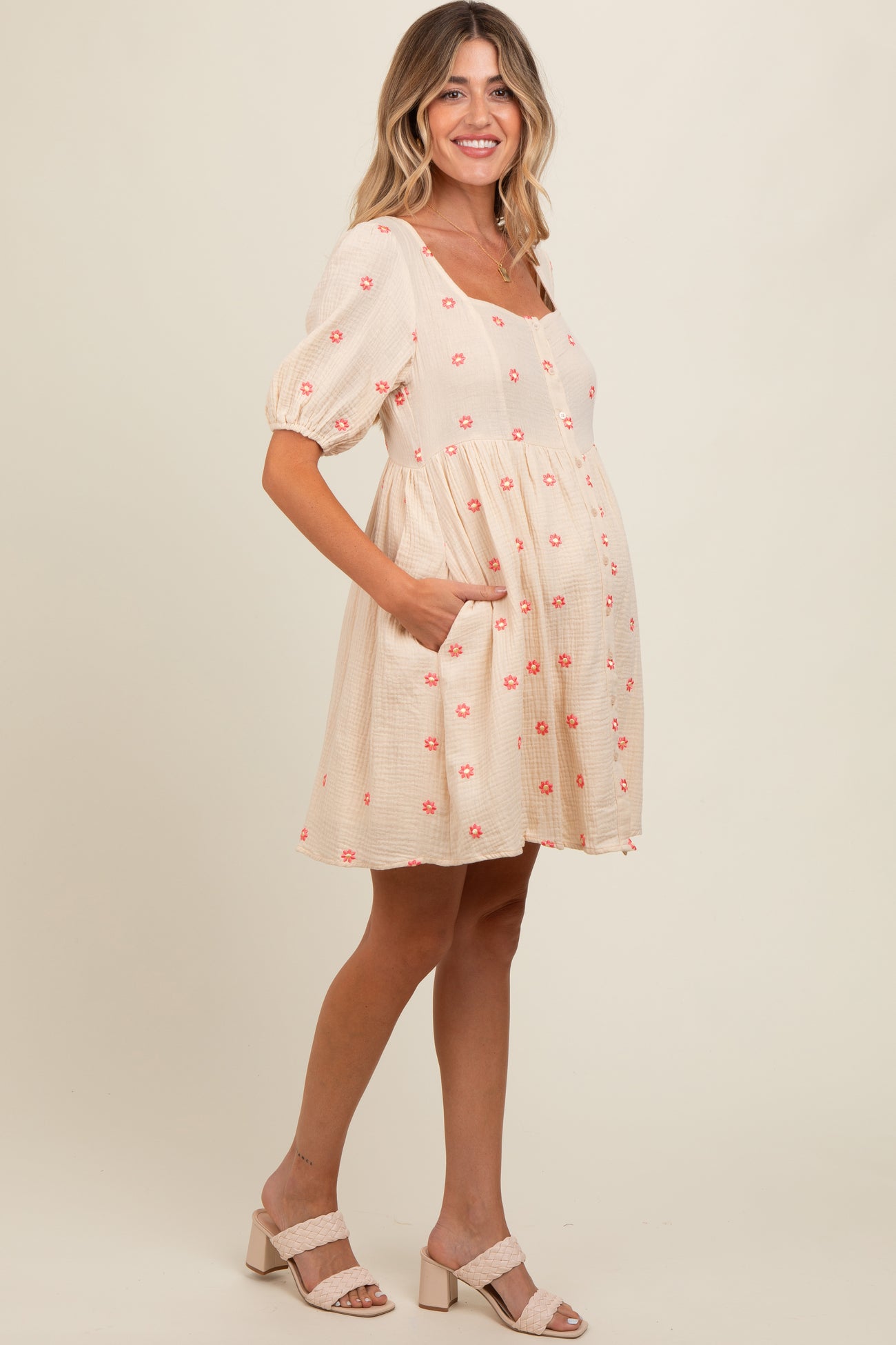 woman wearing a peach maternity dress with floral embroidery and puff sleeves, showcasing her baby bump
