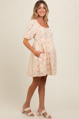 woman wearing a peach maternity dress with floral embroidery and puff sleeves, showcasing her baby bump