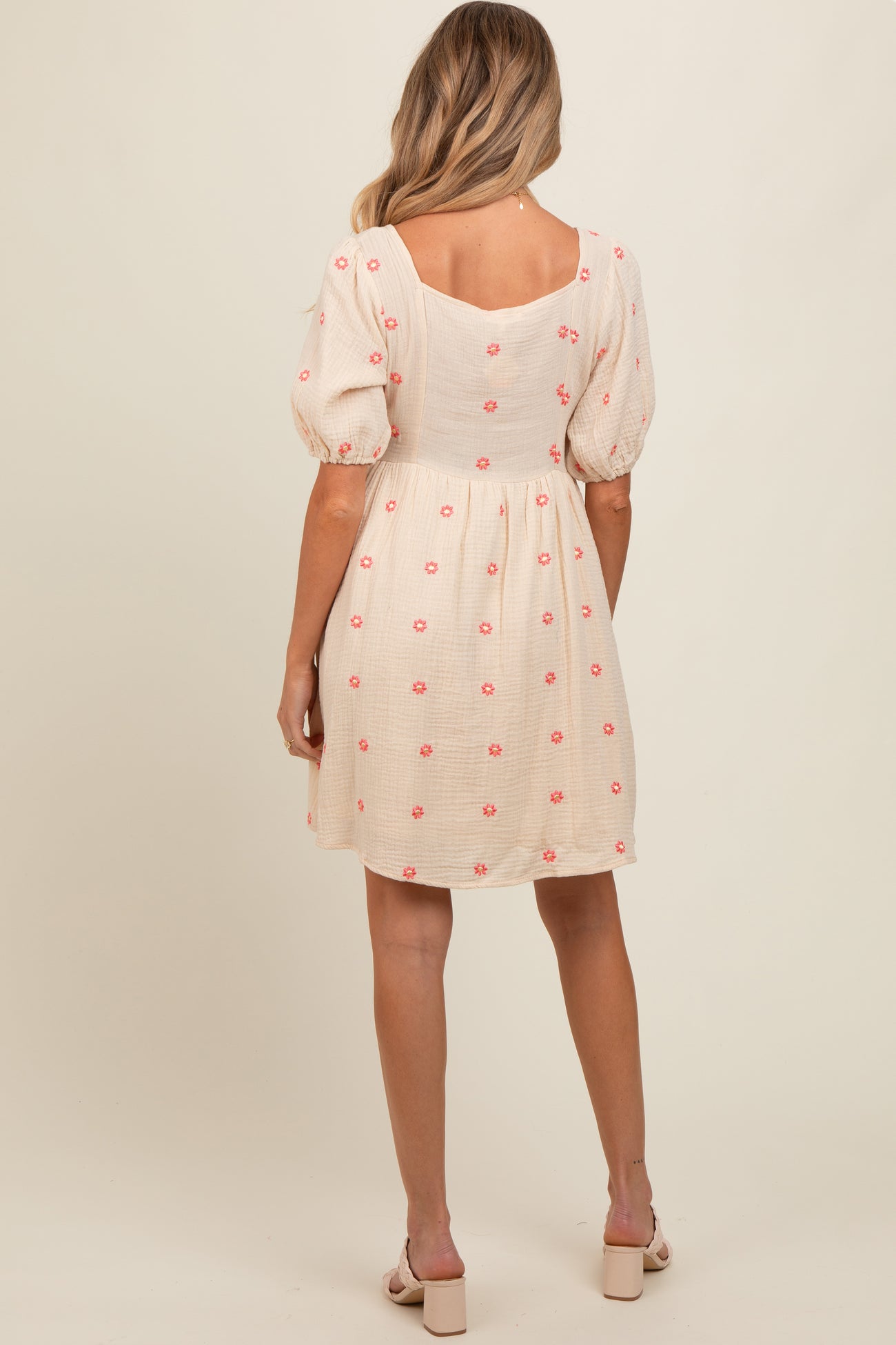 woman wearing a cream maternity dress with pink floral embroidery and puff sleeves, showing a baby bump from the back