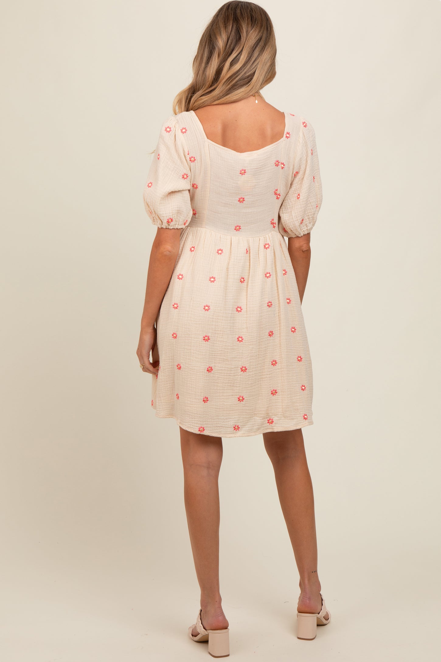 woman wearing a cream maternity dress with pink floral embroidery and puff sleeves, showing a baby bump from the back