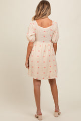 woman wearing a cream maternity dress with pink floral embroidery and puff sleeves, showing a baby bump from the back