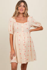 woman wearing a light beige short puff sleeve maternity dress with floral prints and a button-down front